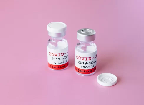 Two bottles of covid-19 vaccine on a pink background.